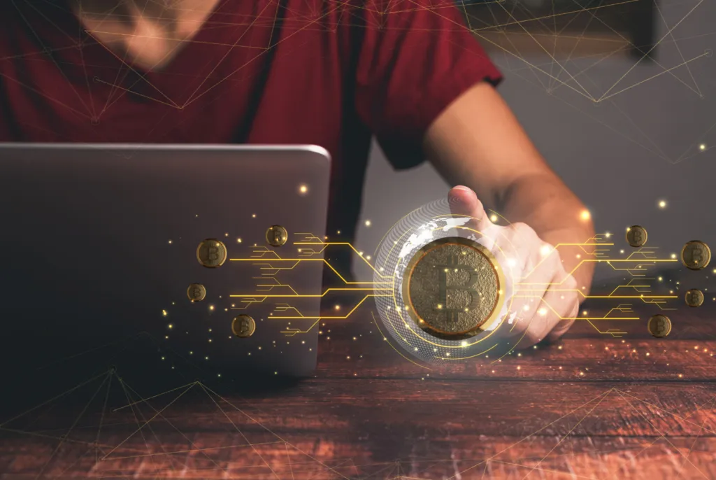 Dizüstü bilgisayar başında kripto para işlemi yapan kişinin önünde Bitcoin ağını gösteren dijital efekt
